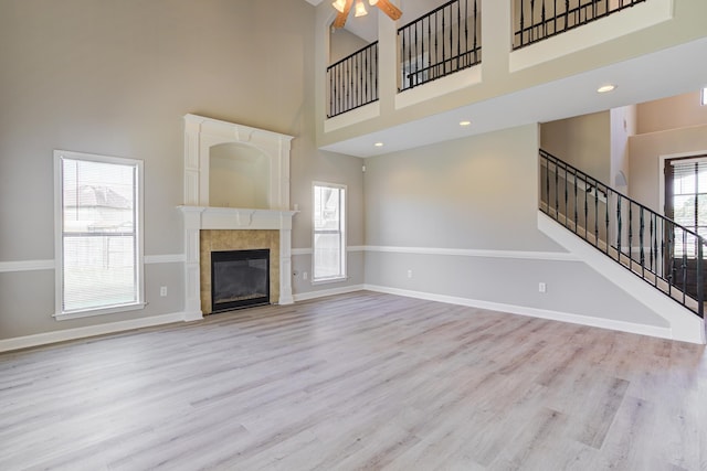 unfurnished living room with a towering ceiling, wood finished floors, stairs, ceiling fan, and baseboards