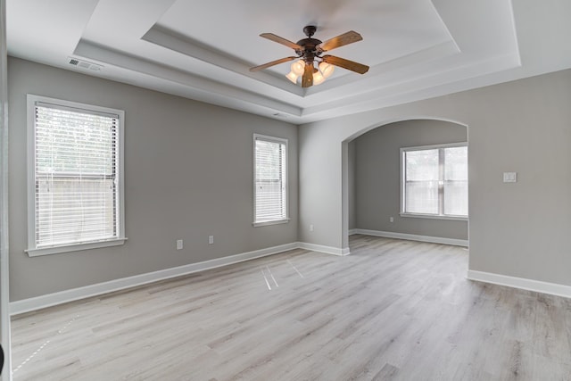 empty room featuring a raised ceiling, arched walkways, healthy amount of natural light, and a ceiling fan