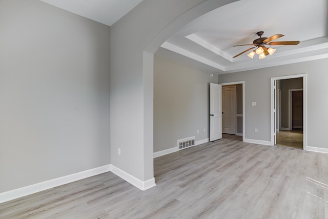 spare room with arched walkways, ceiling fan, light wood finished floors, and a raised ceiling