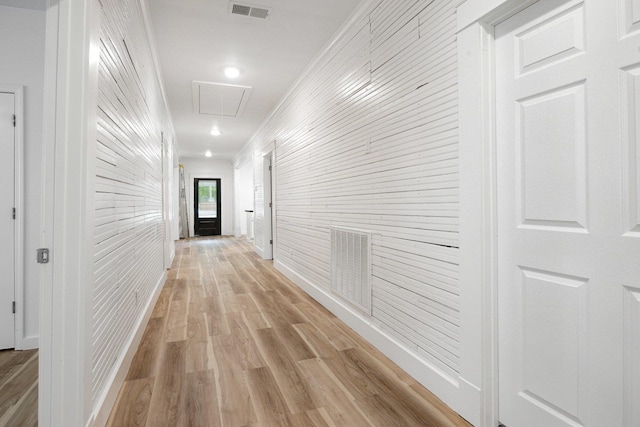 hall with attic access, light wood-style flooring, and wood walls