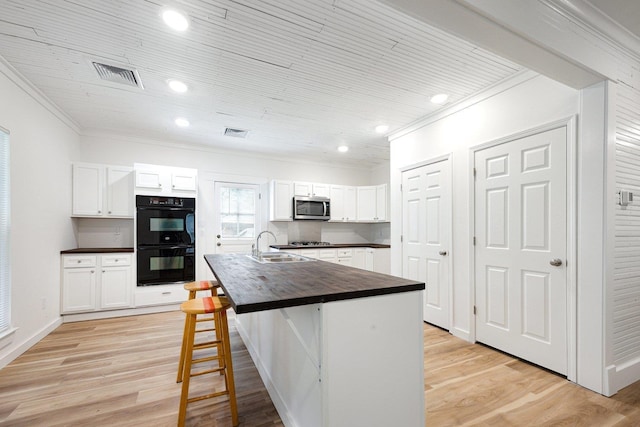kitchen with stainless steel appliances, butcher block counters, crown molding, white cabinetry, and light wood-style flooring