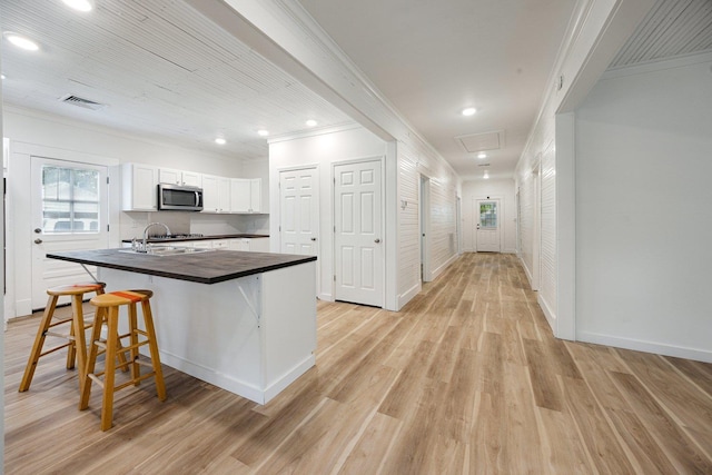 kitchen with stainless steel microwave, ornamental molding, a sink, a kitchen breakfast bar, and light wood finished floors