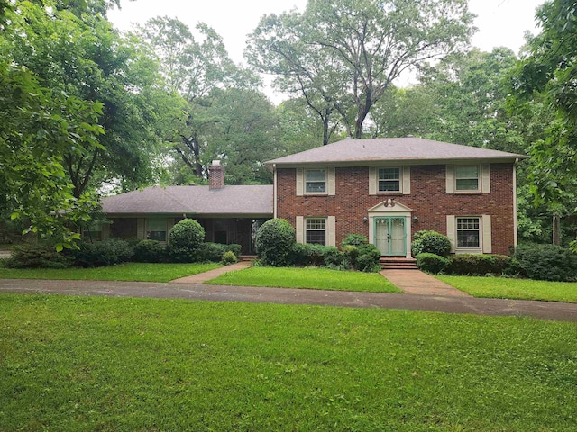 colonial home featuring a chimney, a front yard, brick siding, and french doors