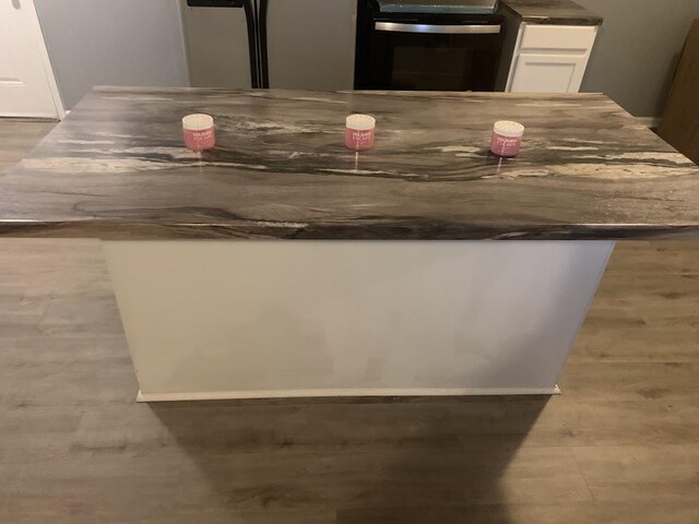 kitchen view of range, white cabinets, dark countertops, and wood finished floors