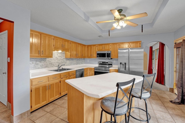 kitchen with stainless steel appliances, a sink, light countertops, light tile patterned floors, and a kitchen island