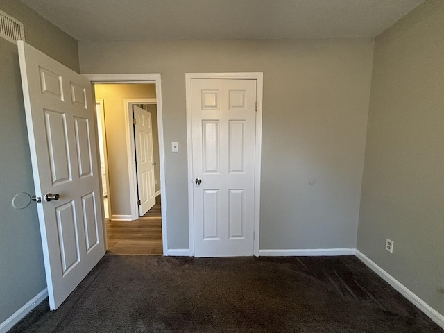 unfurnished bedroom featuring dark carpet and baseboards