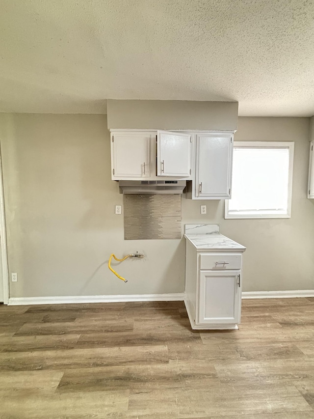 kitchen featuring white cabinets, light wood-style floors, baseboards, a textured ceiling, and light countertops