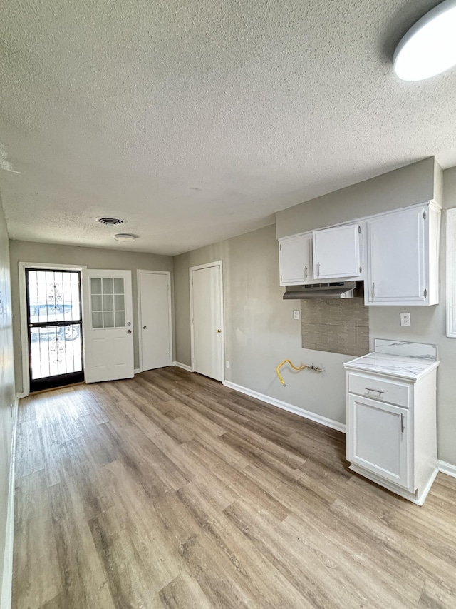 kitchen featuring a textured ceiling, white cabinets, light wood-style floors, baseboards, and light countertops