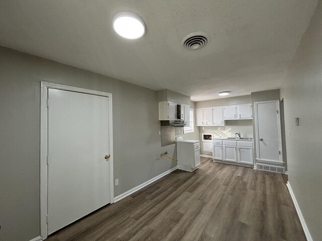 kitchen with a sink, dark wood-style floors, baseboards, white cabinets, and light countertops