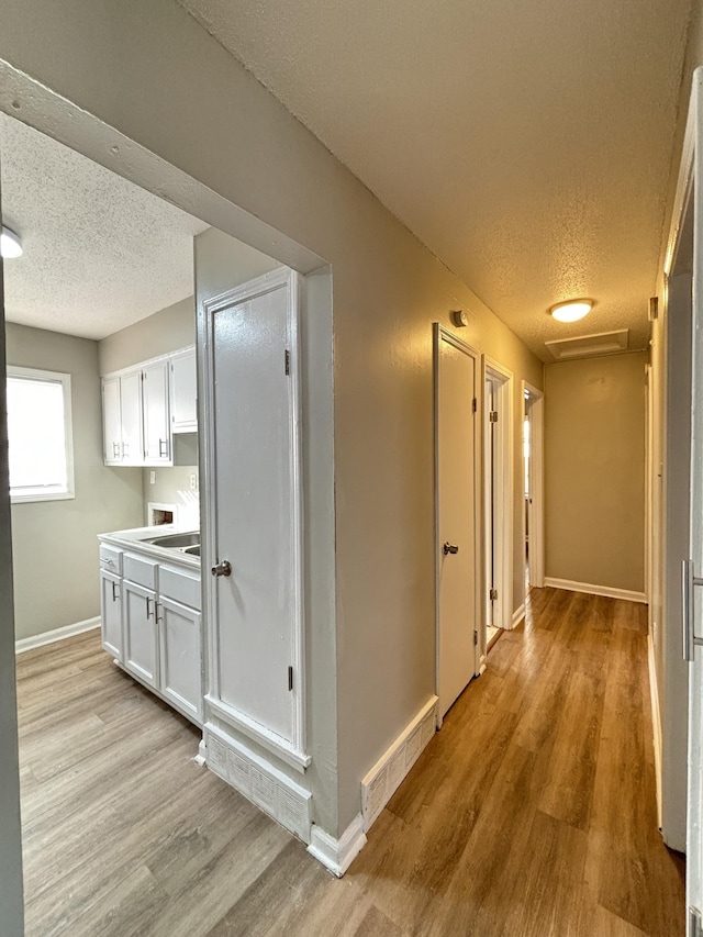 hallway with a textured ceiling, light wood-type flooring, baseboards, and attic access