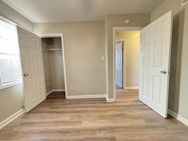 unfurnished bedroom featuring light wood-style floors, a closet, baseboards, and a textured ceiling