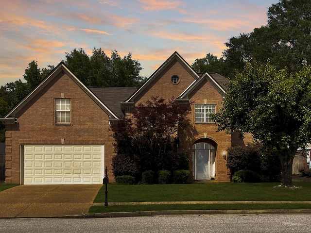 traditional-style house featuring a garage, brick siding, a yard, and driveway