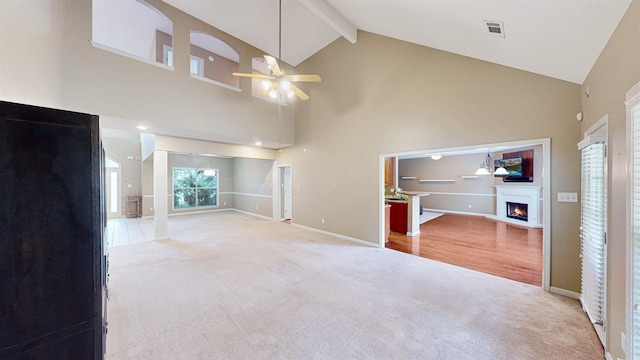 unfurnished living room featuring a warm lit fireplace, high vaulted ceiling, light colored carpet, ceiling fan, and beam ceiling