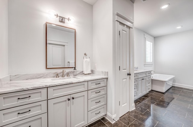 bathroom with baseboards, vanity, a freestanding tub, and recessed lighting