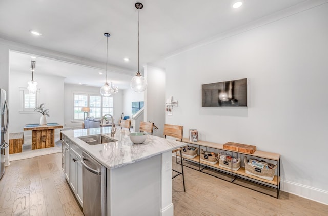 kitchen featuring a sink, appliances with stainless steel finishes, light wood-type flooring, an island with sink, and light stone countertops