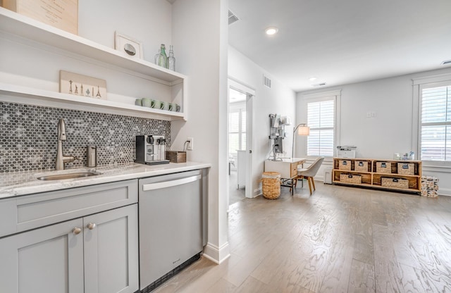 bar featuring dishwasher, a sink, light wood-style flooring, tasteful backsplash, and baseboards