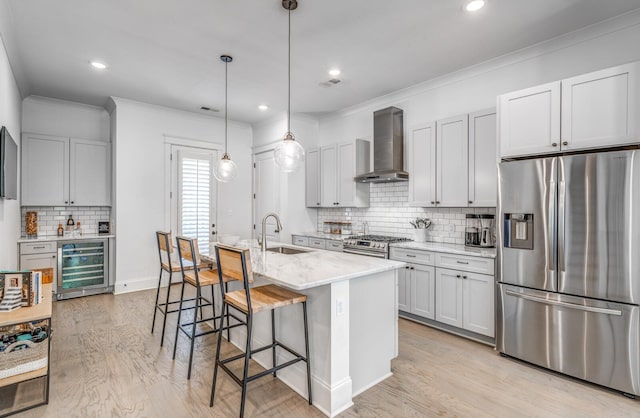 kitchen featuring stainless steel appliances, wall chimney range hood, wine cooler, a sink, and decorative backsplash