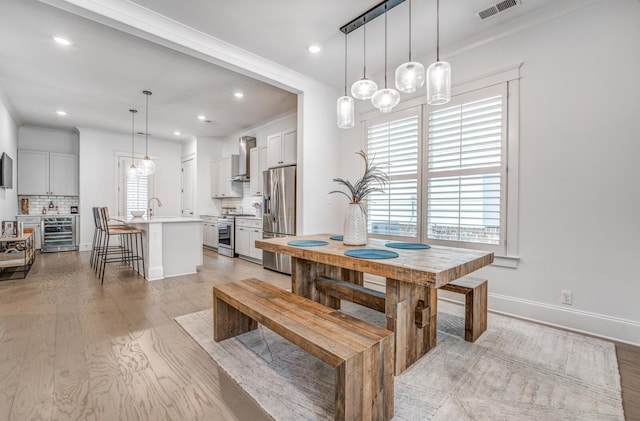 dining area with beverage cooler, light wood-style floors, recessed lighting, baseboards, and crown molding