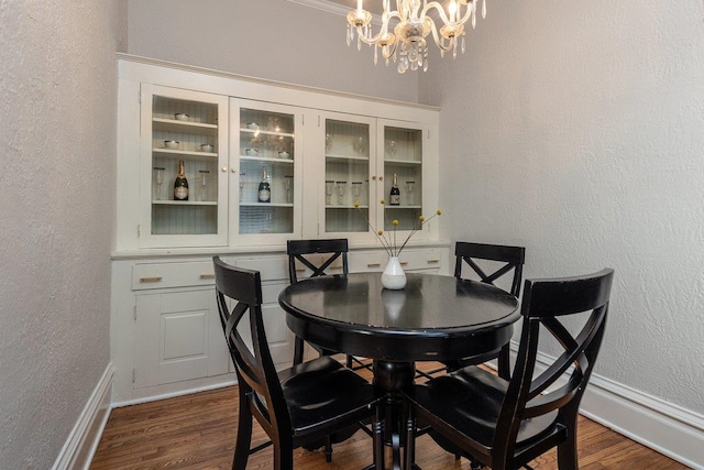 dining room featuring a textured wall, a chandelier, dark wood-type flooring, and baseboards