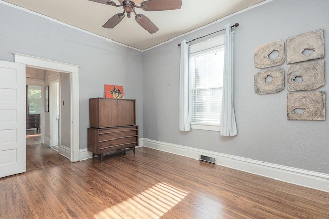 empty room with wood finished floors, crown molding, ceiling fan, and baseboards