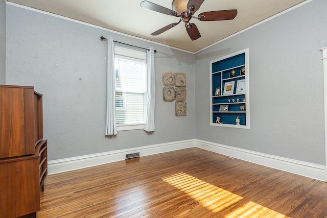 spare room with ceiling fan, ornamental molding, wood finished floors, built in shelves, and baseboards