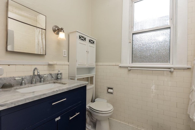 bathroom with tile walls, wainscoting, toilet, vanity, and tile patterned floors
