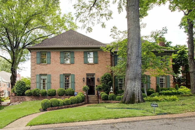 view of front of house featuring brick siding, a front yard, and a shingled roof