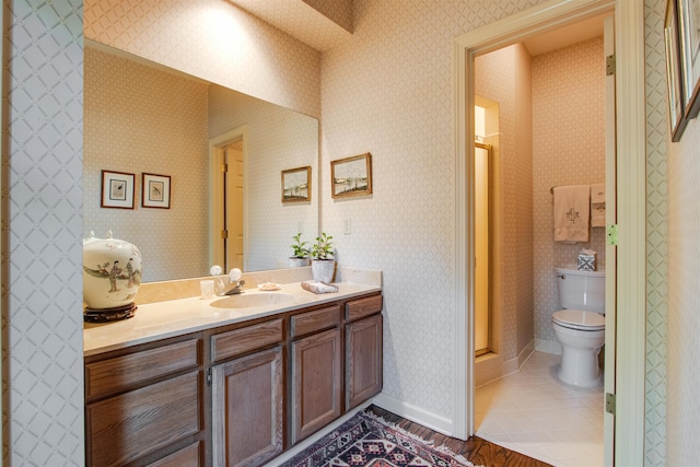 full bathroom featuring vanity, a stall shower, toilet, wallpapered walls, and baseboards