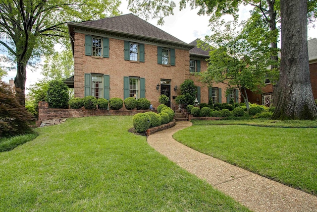 georgian-style home with roof with shingles, a front lawn, and brick siding