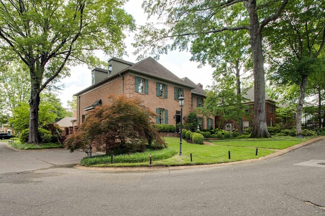 view of front facade featuring brick siding, a front yard, and a chimney