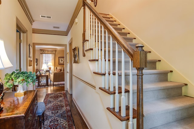 stairway with wood finished floors and crown molding