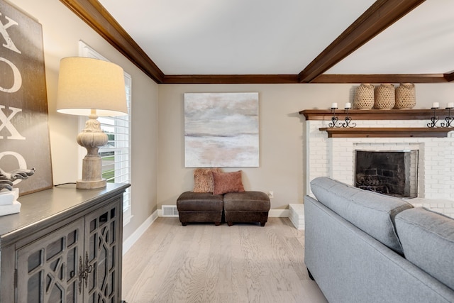 living room with crown molding, baseboards, light wood-style floors, a brick fireplace, and beamed ceiling