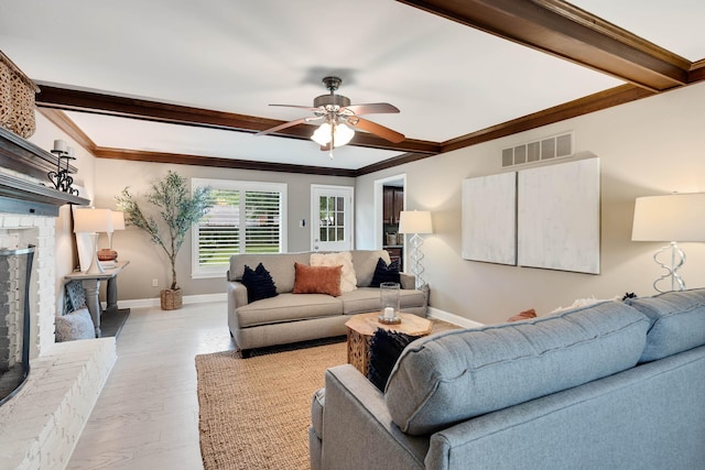 living room with beamed ceiling, a fireplace, ceiling fan, baseboards, and ornamental molding