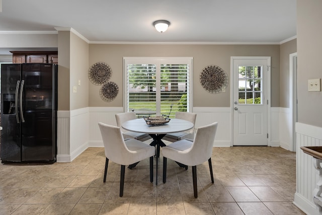dining area with a wainscoted wall, ornamental molding, and light tile patterned floors