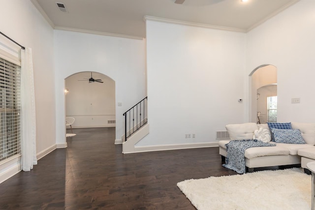 living room with arched walkways, a ceiling fan, stairs, ornamental molding, and dark wood finished floors