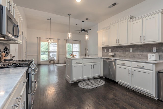 kitchen with stainless steel appliances, a sink, a peninsula, white cabinets, and dark wood-style flooring