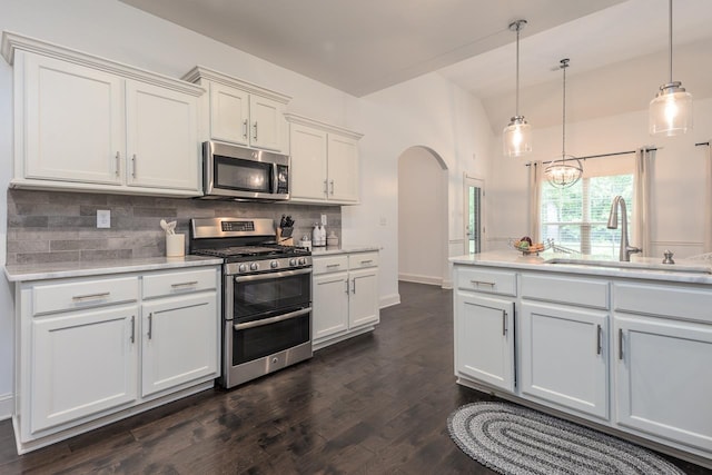 kitchen with stainless steel appliances, a sink, arched walkways, tasteful backsplash, and white cabinetry