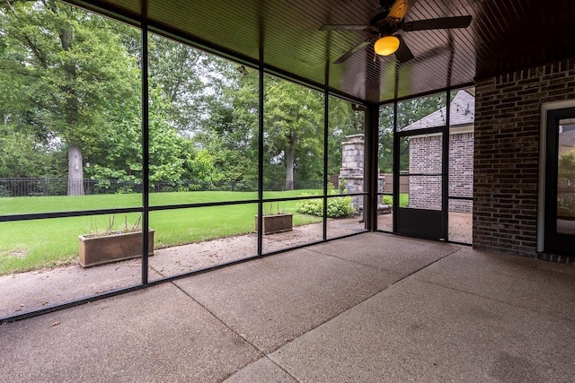 unfurnished sunroom featuring a ceiling fan and view of wooded area
