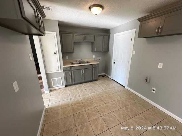 kitchen featuring baseboards, a sink, light tile patterned floors, a textured ceiling, and gray cabinetry
