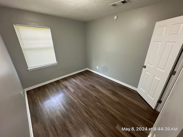 unfurnished room featuring dark wood-type flooring, a textured ceiling, and baseboards
