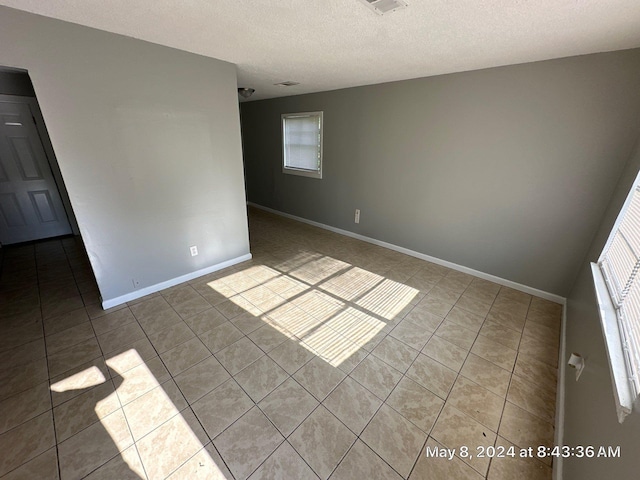 spare room with tile patterned flooring, a textured ceiling, and baseboards