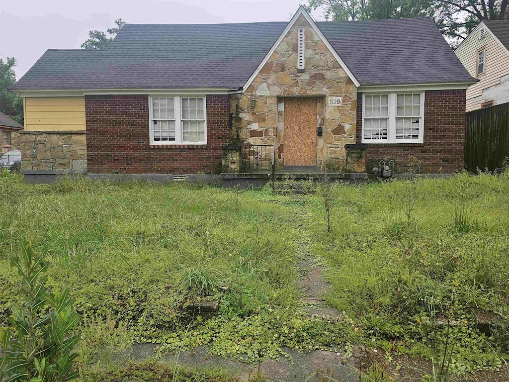 view of front of house with stone siding, brick siding, fence, and roof with shingles