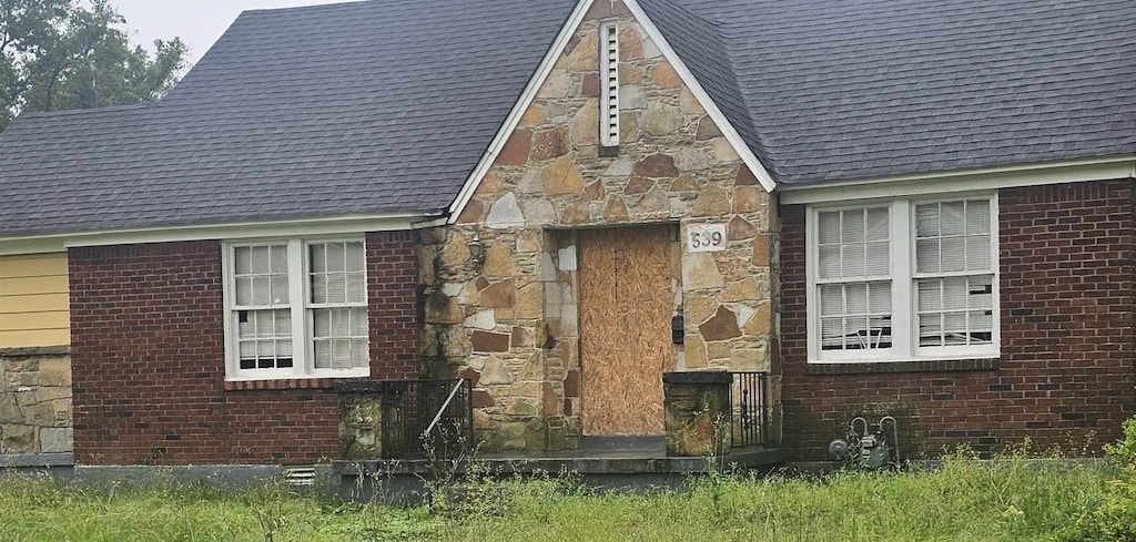 view of side of property with stone siding, a shingled roof, and brick siding