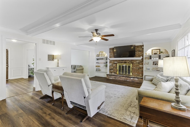 living room featuring crown molding, dark wood-type flooring, beamed ceiling, a ceiling fan, and built in shelves