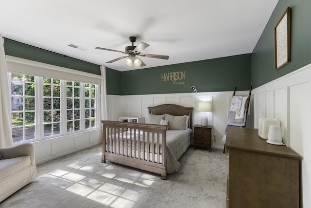 carpeted bedroom with a decorative wall, a wainscoted wall, and a ceiling fan