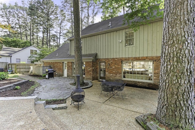 rear view of property with brick siding, a patio area, an outdoor fire pit, fence, and board and batten siding