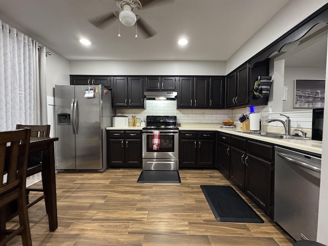 kitchen with stainless steel appliances, under cabinet range hood, a sink, dark cabinets, and ceiling fan
