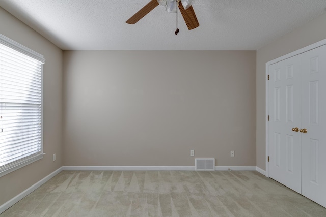 unfurnished bedroom featuring light colored carpet, a textured ceiling, a closet, a ceiling fan, and baseboards