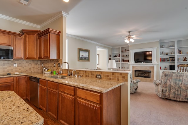 kitchen with a sink, stainless steel appliances, a tiled fireplace, a peninsula, and ceiling fan