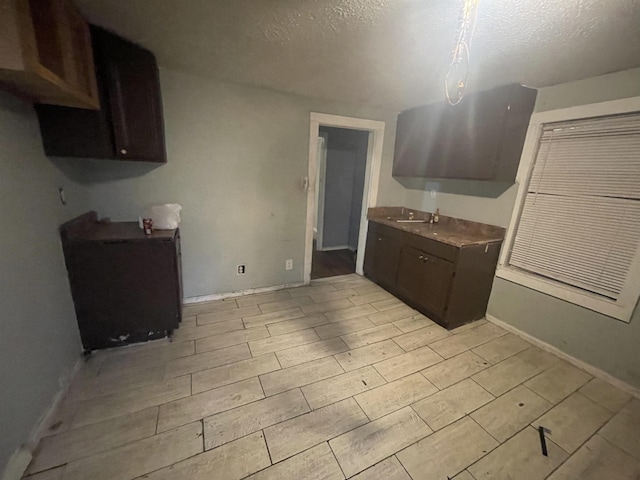 3766 Orchi Rd, Memphis, TN 38108 - kitchen with a textured ceiling, dark brown cabinetry, baseboards, and light wood-style flooring